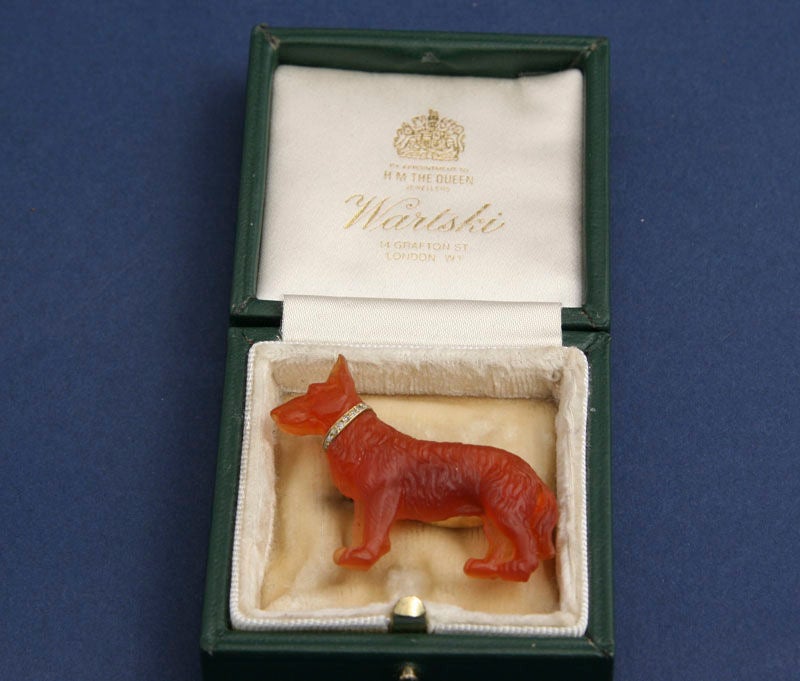 A brooch of a dog, an Alsatian or German Shepard,  in carved carnelian and mounted in 14 karat gold.  The dog is full bodied, with deeply carved fur and a collar of nine small diamonds.  He is hallmarked on the back with the maker's mark and the