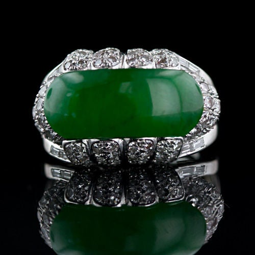 A large, impressive, deep translucent green, saddle shape natural jadeite set in platinum and diamonds. The jade is lavishly presented in a handmade platinum mounting with diamond set scallops and double tiered shoulders with baguette diamonds set