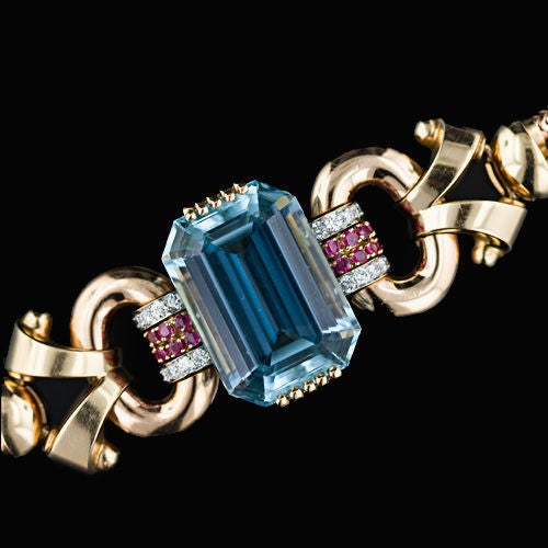 Retro at it's best! This incredible bracelet features a 46 carat large emerald cut aquamarine with an even blue color nestled between dimensional oval links and scrolls attached with a band set with rows of rubies and diamonds. A double row of snake