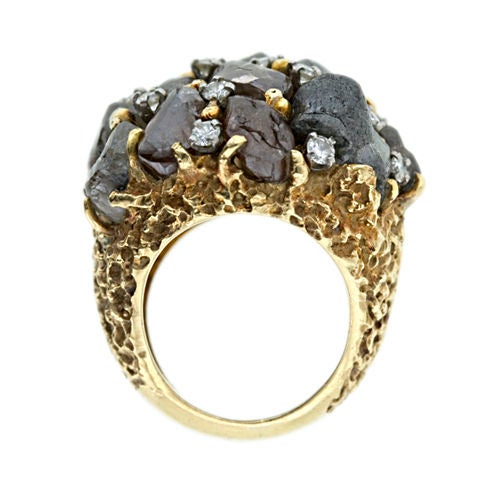 A true Art piece from the 1960s. Fifteen rough diamonds in shades of brown to grey create a dramatic look. The ring is brightened with sixteen round brilliant cut diamonds dotted throughout. This 18K yellow gold ring has an organic gold nugget