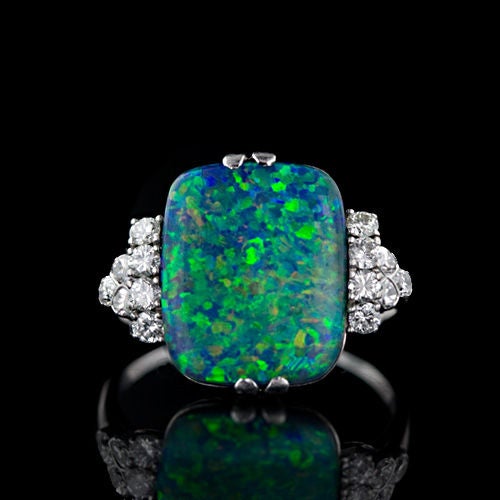 This 5.80 carat black opal displays electric play of color in a soft cushion shape. The confetti like pattern is predominantly green and blue with a touch of yellow and orange. It is flanked by round brilliant and marquise cut diamonds. A delightful