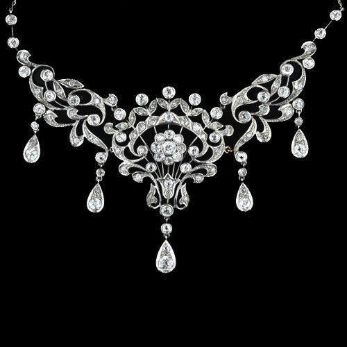 This antique bib style necklace from the 1890's is very early Edwardian. The floral and scroll motifs are fully diamond set with five pear shaped diamond set pendants. As with many pieces made at this time you can also see the influence of the Art