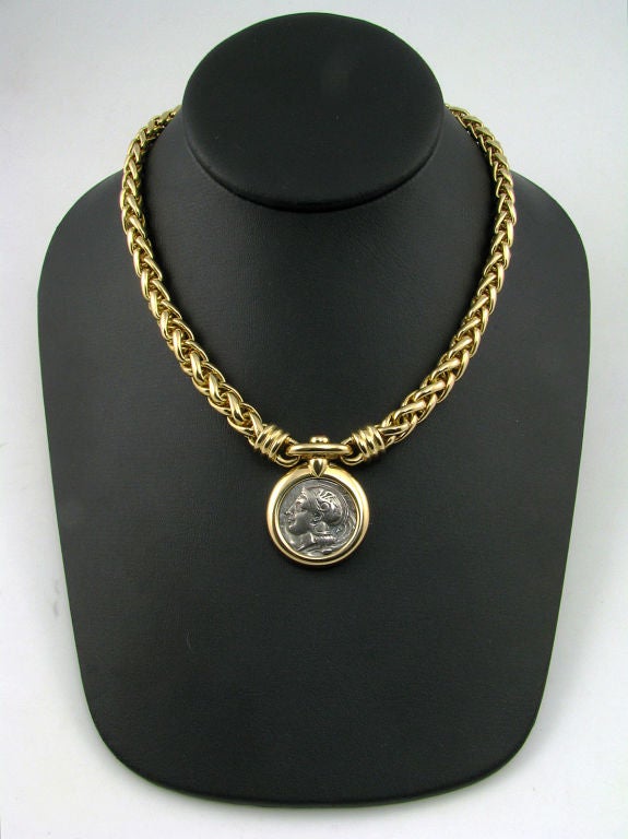 An 18 karat yellow gold, coin and ruby necklace:<br />
- signed Bulgari<br />
- woven chain link suspends an antique coin of a warrior on one side and a lion on the other<br />
- bezel surrounding the coin is engraved on the back with Lucanie