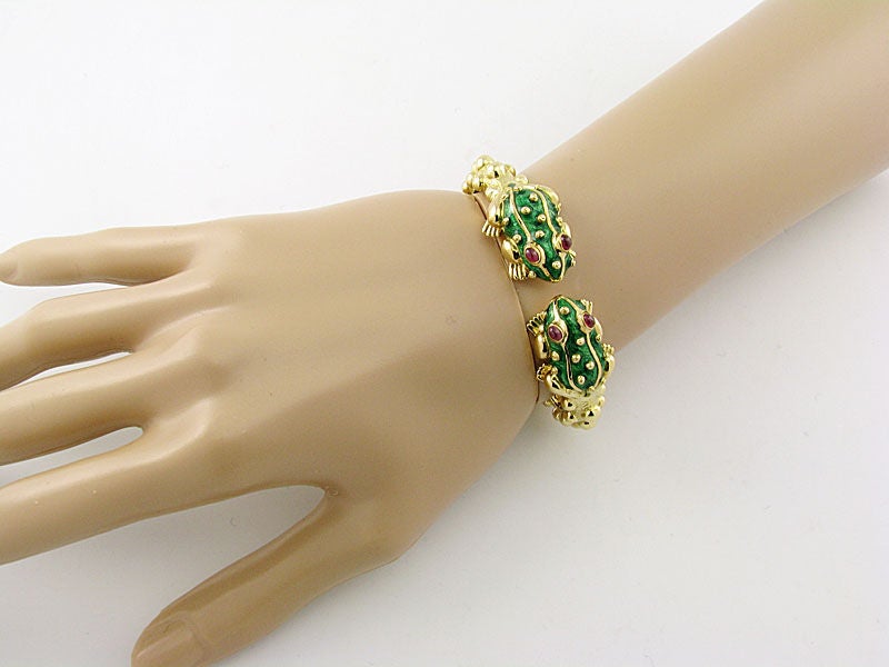 An 18 karat yellow gold and green enamel frog bangle with ruby eyes by David Webb.  Designed as a hinged open bracelet with <br />
green enamel frogs, yellow gold dots and cabochon ruby eyes.