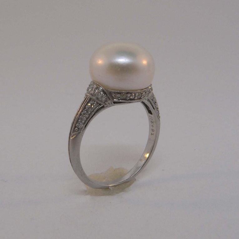 An Art Deco pearl and diamond ring by JE Caldwell & Co set with a natural button-shaped pearl weighing 8.03 carats mounted to a platinum ring set with 38 brilliant-cut diamonds to a millegrain setting.  The ring is signed 'JEC & CO' and is numbered