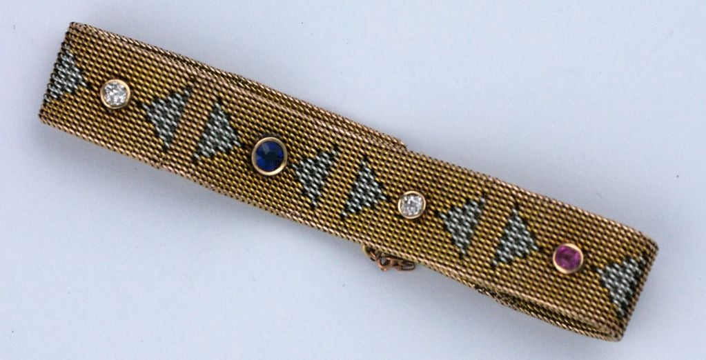 This unusual and elegant 2 tone Deco mesh band bracelet is woven with triangular motifs between bezel set stones. Realized in 14k white and yellow gold, the art deco pattern includes a patriotic mix of rubies, diamonds and a singular sapphire. <br