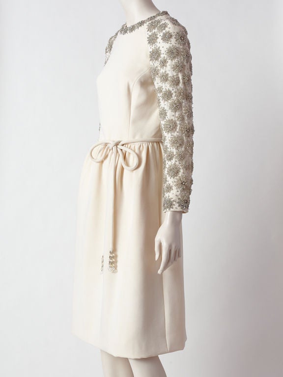 Ivory, fine wool crepe cocktail dress with crystal beading detail, circa 1960's. Fitted bodice with slightly gathered skirt. Jewel collar and raglan sleeves are encrusted with sculpted crystal beaded clusters and rhinestones that form a 