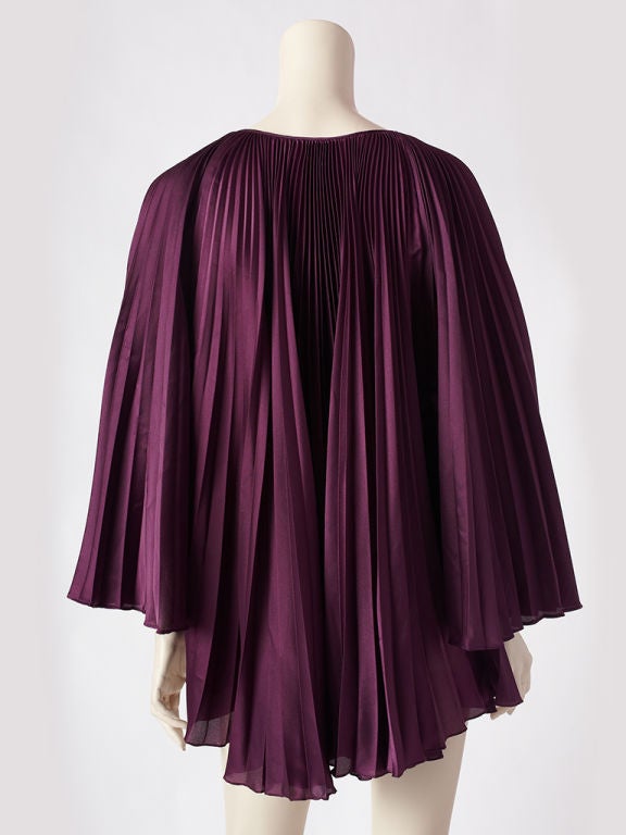 Mollie Parnis plum colored crystal pleated tunic. Body and wide   bell shaped sleeves are pleated. Neckline is open with side <br />
tie detail.