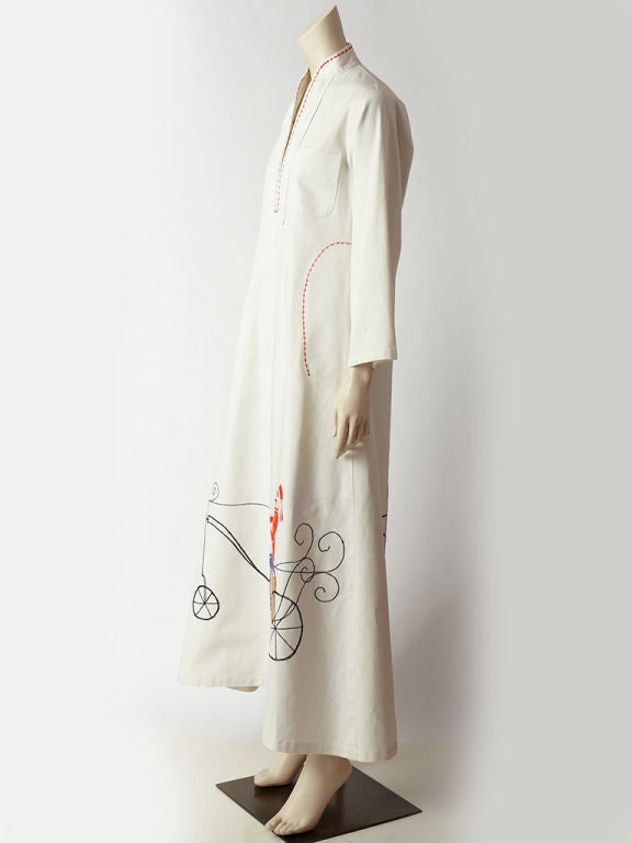 Serendipity white denim, long sleeved caftan with colored embroidered detail along neckline and pockets. Whimsical, figurative, carriage and bicycle  themes are embroidered and appliqued along the hem line.