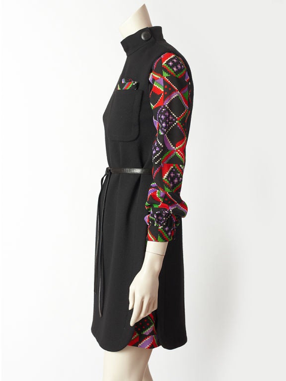Pierre Cardin 2 piece dress consisting of a black, wool knit, high neck, sleeveless jumper with slits up the waist exposing the wool challis geometric pattern long sleeve dress underneath. Jumper has a breast pocket with small pochette made of the