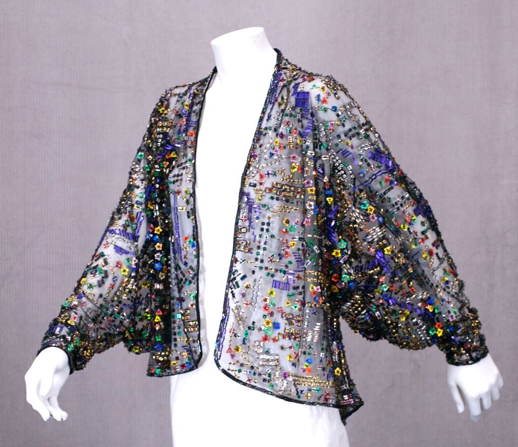 Halston Black Tulle evening jacket embroidered with multicolored paillettes and beads. Unusual form paillettes and floral sequins are spaced around a colorful,festive map pattern. 
   Sleeves are a unusual lobe shaped kimono sleeve with a tapered