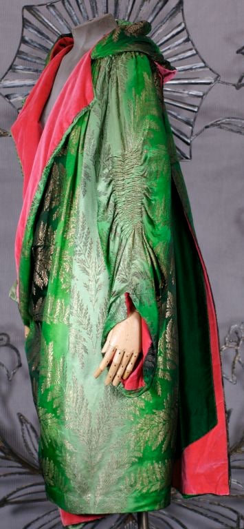 This is a lovely opera coat circa 1920 of lame broche in ombred shades of green with gilt lame leafy fern motifs reminiscent of Chanel's kimono coats of obi silk. It is lined in a vibrant coral silk velvet and the combination is stunning.<br />
 