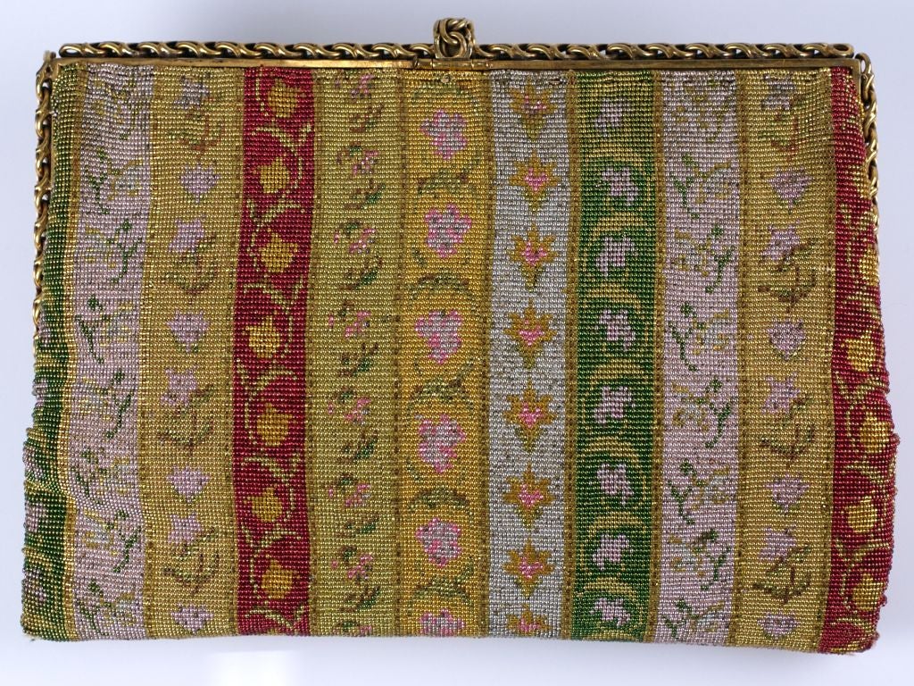 This 1930s deco french clutch has an intricately beaded pattern of florals within beaded color bands. The microbeading is comprised of gold, yellow,pink, green and ruby beads. The frame is edged in gilt chaining.<br />
Lined in gold silk satin.<br