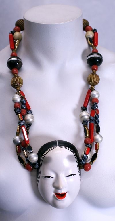 Striking necklace composed of semiprecious and glass beads centered on a porcelain hand painted Noh mask. Unusual glass beads and pearls interdispersed with ribbed brass spacers and semiprecious tumbled stone beads. Statement necklace 1980s.<br