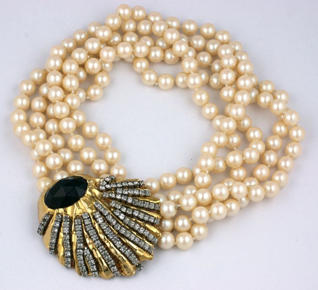 Striking faux pearl necklace with hammered gilt clasp set with contrasting rows of rhinestones in silvered settings. A large rose cut facetted sapphire stone centers the clasp.<br />
5 strands of 10mm pearls.   16