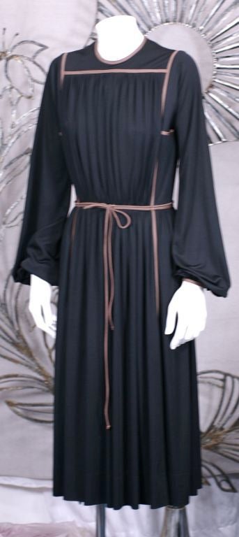 Black jersey dress with taupe piping by Donald Brooks. Austere minimalistic feel with gathered bodice which releases into a full gathered skirt. A double wrap taupe piping belt covers the waistline. Back zip entry. <br />
Excellent condition.