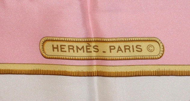 This is a collectible 100% silk pink, cream, gray, and gold scarf by Hermes, from the 1980's. The scarf has rolled, hand sewn edges, and comes with the original box and cards. There are a few of very tiny and undetectable stains. It measures 35