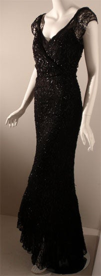 This is a black sequin and silk 2pc gown, custom made from the 1940's. It has short sleeves, layers of ruffles at the hemline, hidden snaps up the side seam, and a deep 