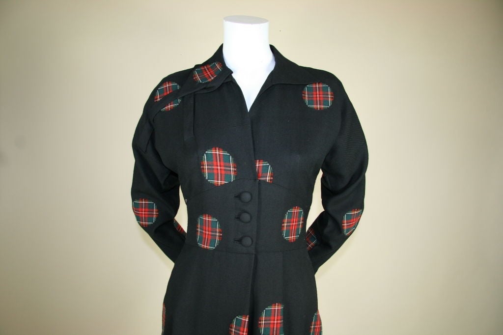 1940s wool dress with full length sleeves, and tartan circular patches. Fitted cumberbund waist with three covered buttons, three pleats on the left, self trim on the top right that wraps around collar, full length sleeves. Length of dress falls
