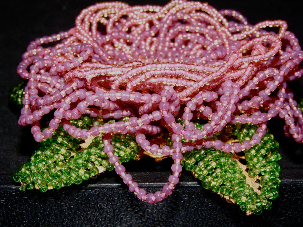 Ian St.Gielar oversize beaded flower brooch. Gold decorative circular back with leaves, green beads over the leaves. A mix of purple and pink strings of beads making the flower, a center of pink rhinestones and a small pink resin flower with