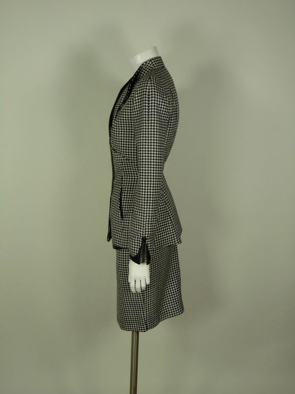 Mugler wool hounds-tooth skirt suit with leather detail. Classic Mugler 1940s inspired skirt suit. Jacket has shoulder pads and black leather detail on the lapels, across the bust, the hem of the jacket and the hem of the cuffs. The buttons down the