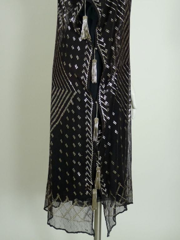 Assuit tunic style dress, black with silver metal. Open seams down the sides with tarnished silver metallic tassels. Length falls below the knee. Geometric coptic pattern with square flecks on majority of fabric. (Slip not included)<br />
<br