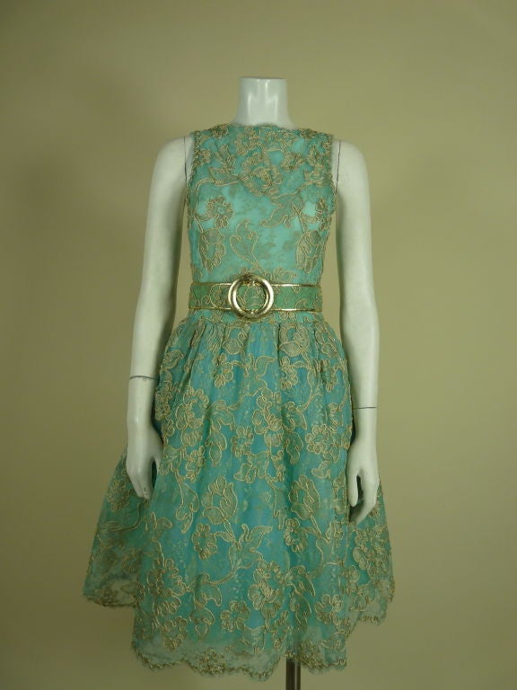 Robin's egg blue lace Scaasi dress embroidered with metallic gold floral motif allover. Gold bullion soutache outlining of flowers, leaves and scalloped hem and neckline.  Lined with tulle and organza petticoat. Belt trimmed in gold leather.<br