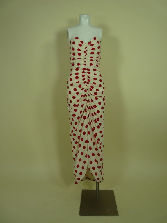 Red on white polka dot strapless silk crepe gown with matching jacket from Arnold Scaasi. Dress is ruched in center from sweetheart neck to petal-like hem. Jacket is sleeveless and closes at neck and waist. Fabric is gathered for fullness. <br