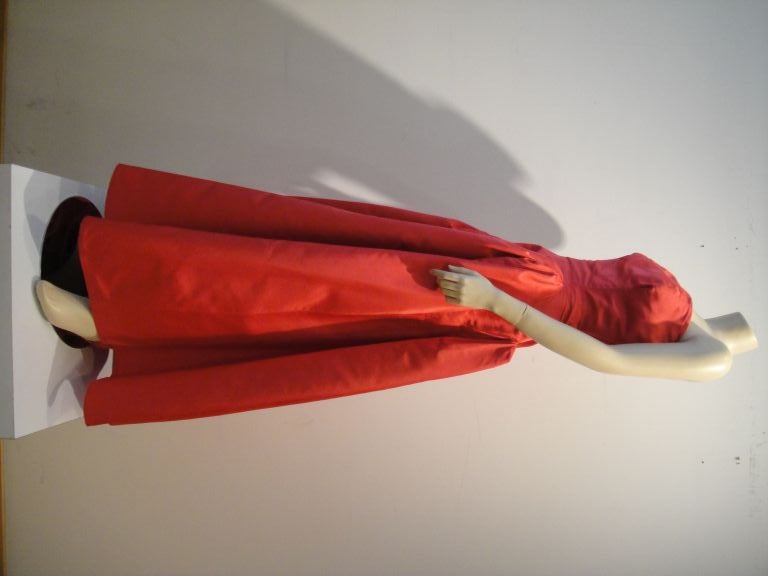 This striking Pauline Trigere strapless asymmetrical 1950s silk taffeta gown in a fresh reddish pink color is intricately structured with double layered bodice, a double zipper, and a weighted lining.  It also includes a matching taffeta wrap not