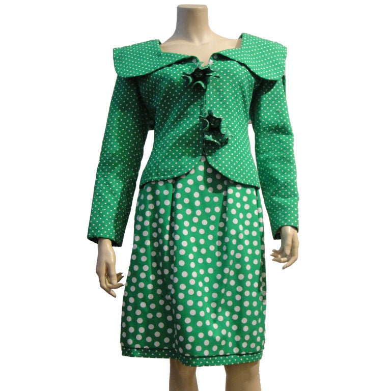 This Galanos '80s green/white polka dot silk skirt suit zips up the front with a wide-cut sailor neckline and sculptural leaf appliques on the front. The skirt features coordinating polka dot print and pleating with a high sculpted waistband.