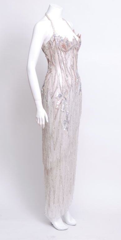 Nude mesh dress with all over beading and sequins, halter neckline, with an underwire bra, boned bodice, side slit in front. The lower part of the gown is fringed with clear silver backed bugle beads.