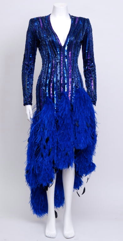 Stunning Bob Mackie blue bead and blue iridescent sequin mini dress with blue ostrich and black iridescent plumes. The dress has long zippered sleeves, plunging neckline, and feathered boa strips falling from the lower hip. The dress is fully lined
