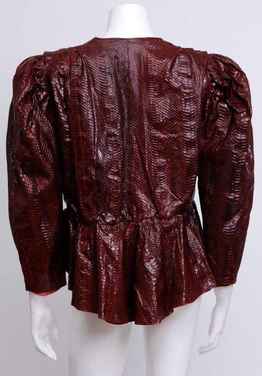 This 1980's glossy maroon snakeskin jacket features large shoulder pads and puffed stylized shoulders,  peplum waist with elastic band and clasp, fully lined.