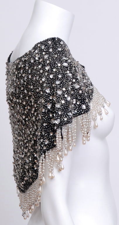 This mini capelet is encrusted with rhinestones, sequins, glass beads, and pearls. The pattern is intricate and perfect to be worn over any dress or outfit. <br />
<br />
Snap Closure.<br />
Shoulder width: 18