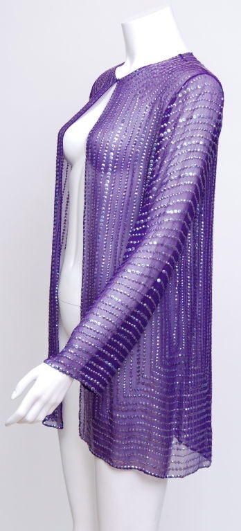 This Halston sheer jacket has a crew neck with a hook and eye closure and is adorned with purple mirrored sequins. Matched perfectly over casual and evening clothing.