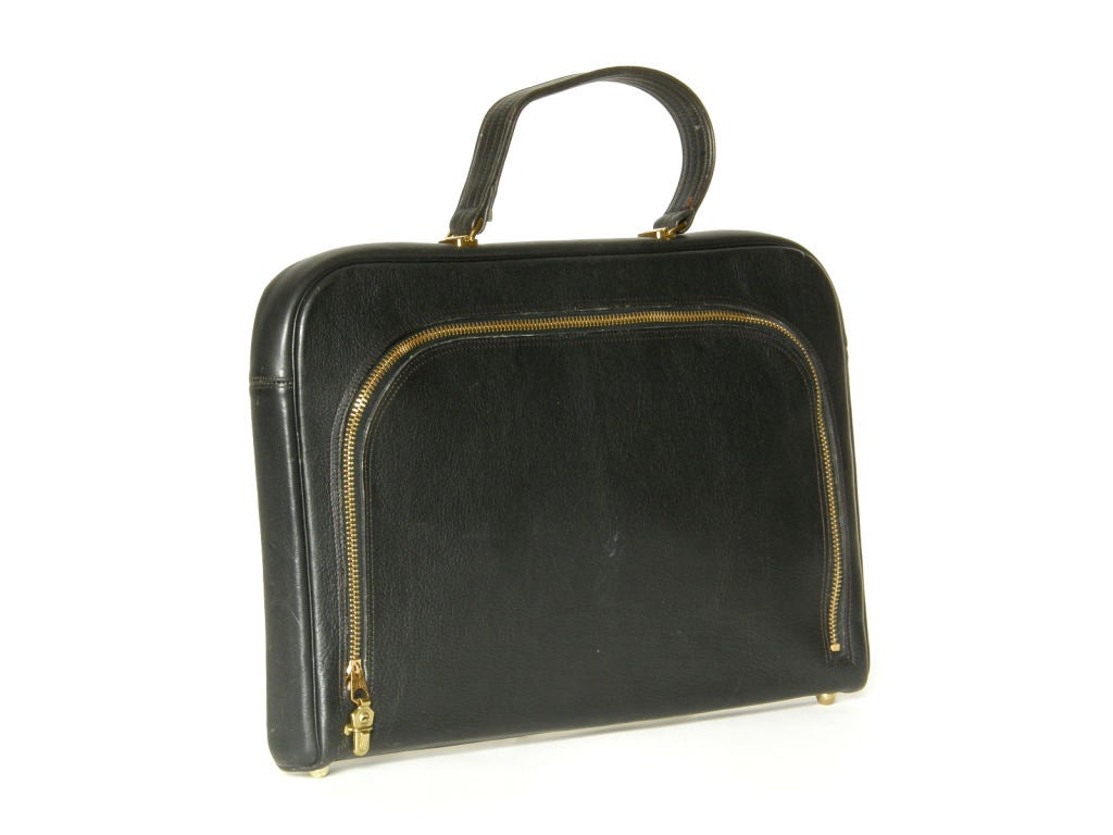 This black leather briefcase style bag designed by Bonnie Cashin for Coach is new/old stock. The main body of the bag opens with a big brass zipper, and the original, stiff paper liner is still inside. On the other side of the bag is an attached