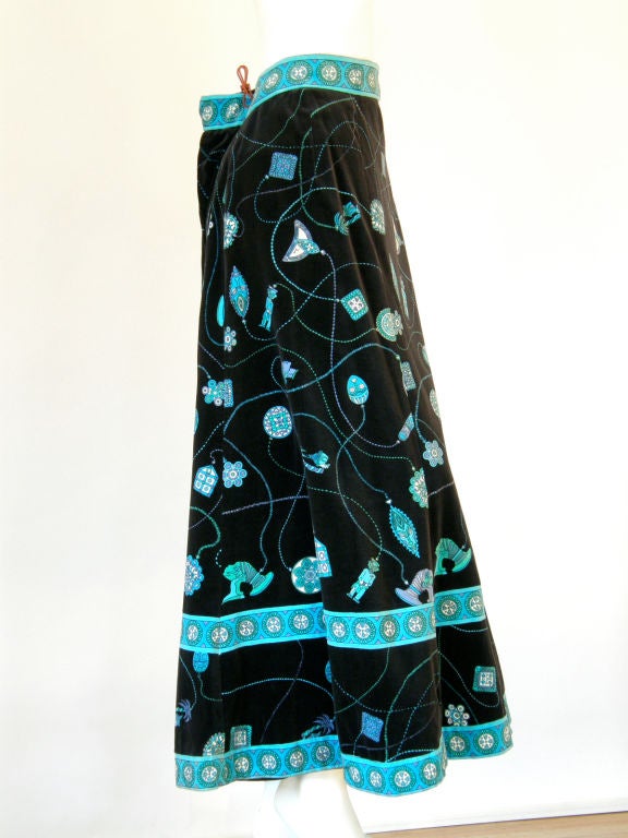 This evening length Pucci skirt is made of black background velveteen printed with bright blue and green exotic, island theme jewelry. There are geometric and tiki style charms hanging from various styled chains. The fully-lined skirt has a gentle