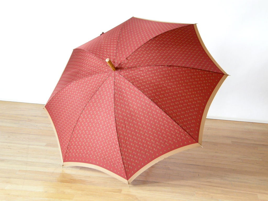 This vintage Gucci umbrella comes in its original box. It has a classic Gucci look, having burgundy and tan fabric printed with bridle imagery and the Gucci name. The bent bamboo handle has a gilt metal, bridle-shaped accent wrapped around it. The
