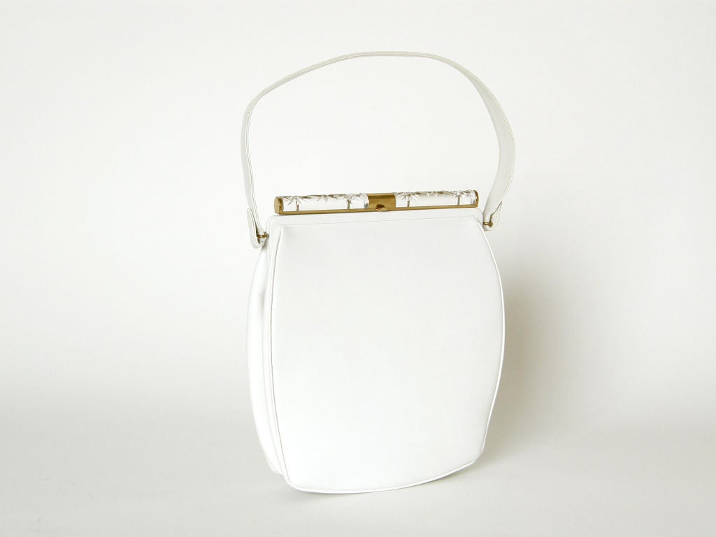This chic, white leather handbag by Holzman features a lucite bar along the top with carved starbursts that sparkle in the light. The lucite bar is framed by gold-plated metal and acts as the clasp, which has a small tab at its center to assist with