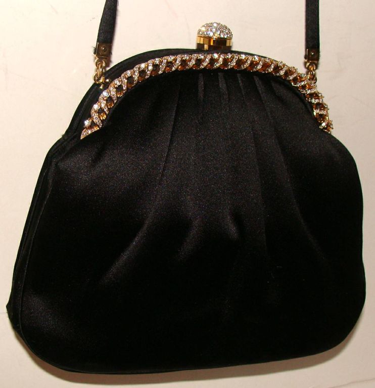 This elegant black satin bag has a brilliant rhinestone frame and clasp.  To open, the wearer pushes down on the top of the clasp.  The evening bag can be used as a clutch or hands free by using the fold in shoulder strap.  (Note:  photos do not