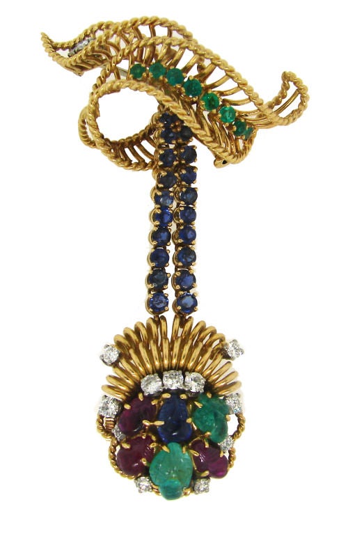 Fabulous colorful brooch was created by Gubelin in 1950's. It is made of 18k yellow gold and set with round brilliant cut diamonds, round cut and carved emeralds and sapphires and carved rubies. The designer artfully hid a mini watch inside of the