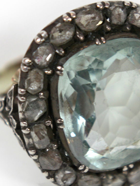 The center aquamarine is a pale to medium color. It's surrounded with 19 early rose diamonds, set in white gold with a gold-colored gold back.