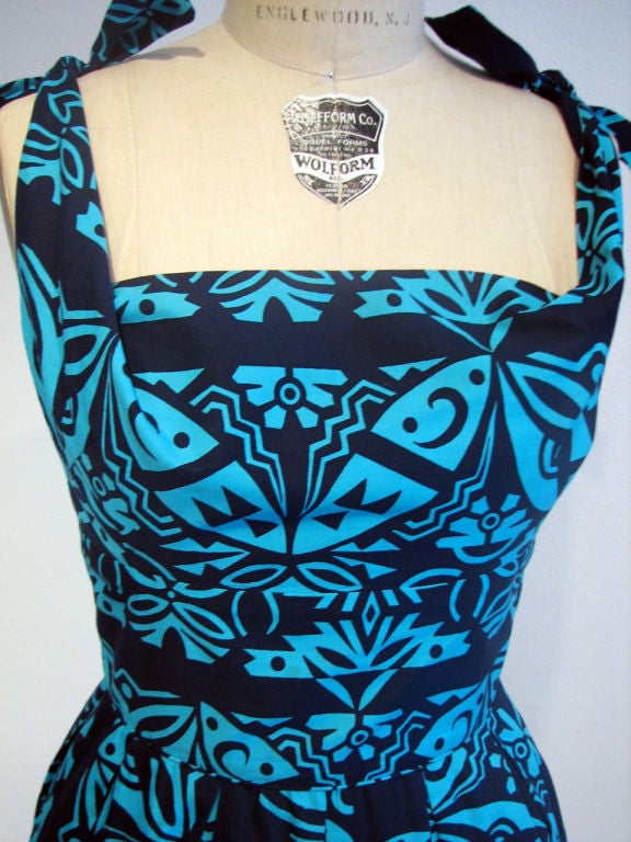 Fine & rare vintage Alfred Shaheen Hawaiian print cocktail dress. Authentic item made in Hawaii. Outstanding & vibrant print (navy/turquoise) item ties at shoulders & zips up back. Item features 'shelf' bust line, nipped waist & full skirt.