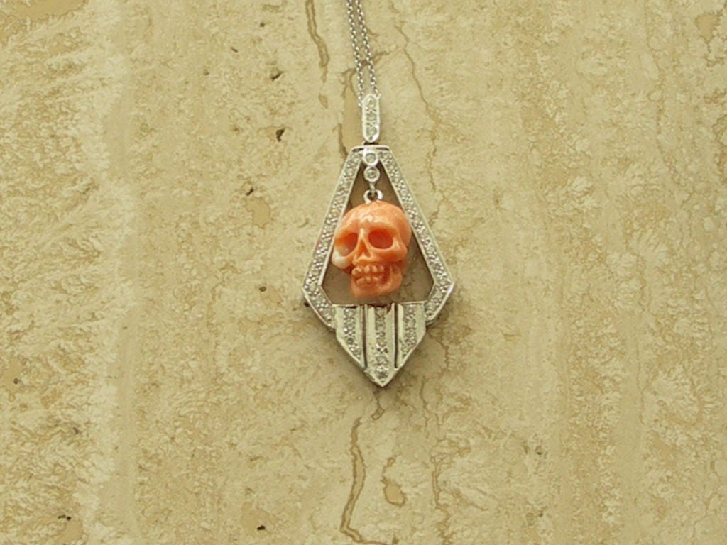 Art Deco style coral skull pendant in diamond chevron shaped frame.