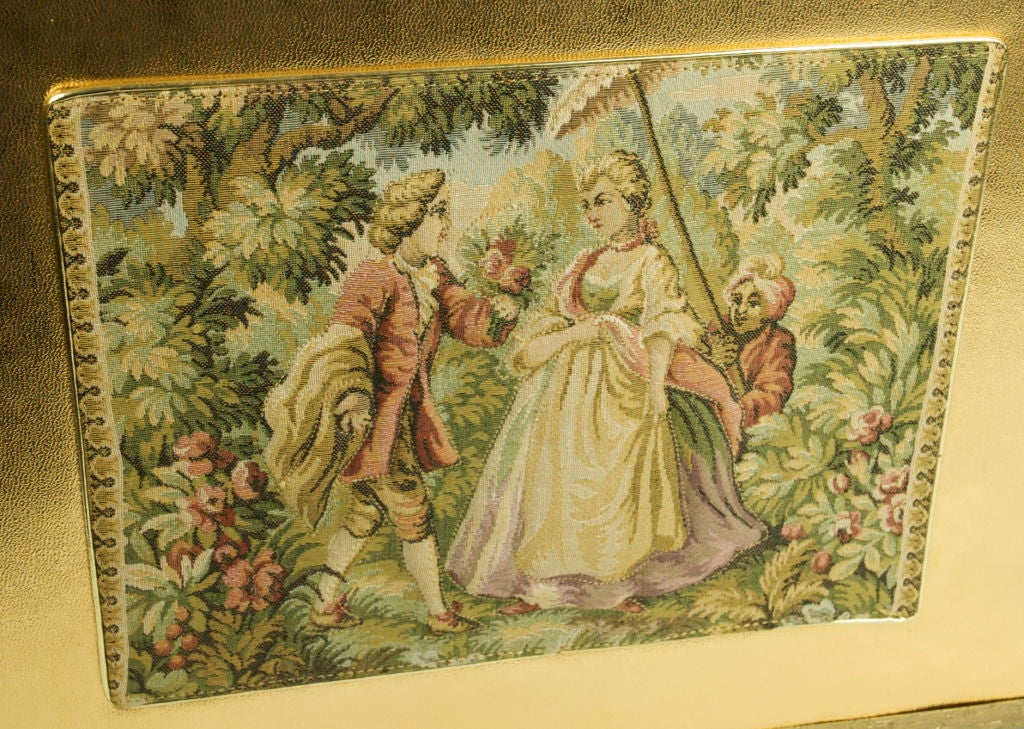 Featured is a huge gold metallic and tapestry hand bag. The French courting figures are raised tapestry while the background is flat.  The hand bag has a gold tone metal around the bottom and the top. It has a clear lucite closure. It is signed and