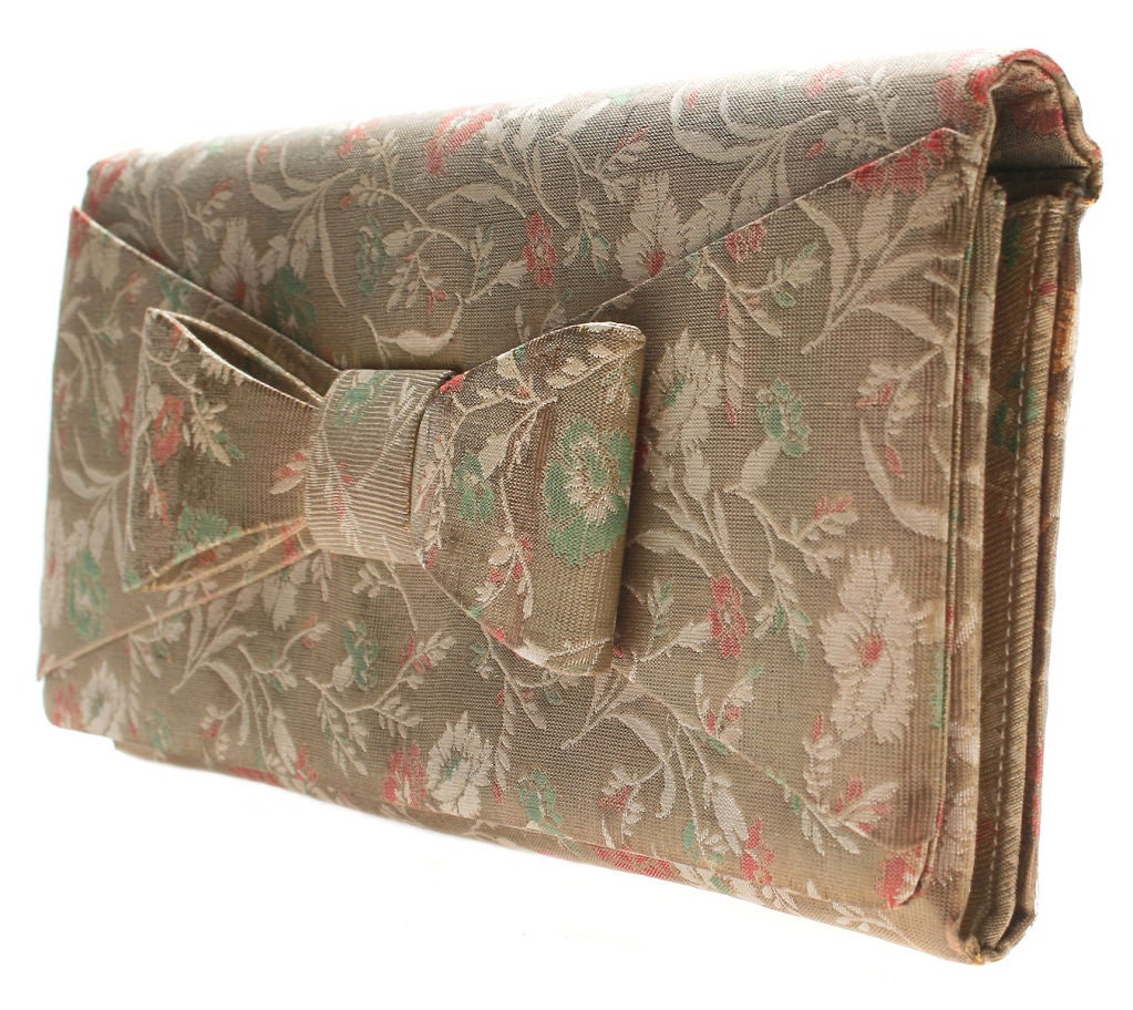 This is a wonderfully patterned clutch in a flat brocade accented with a bow closure. It has an interior zippered compartment and measures 5 inches high, 10 1/4 inches long and is 1 inch in depth when closed. The clutch opens to 3 inches deep.