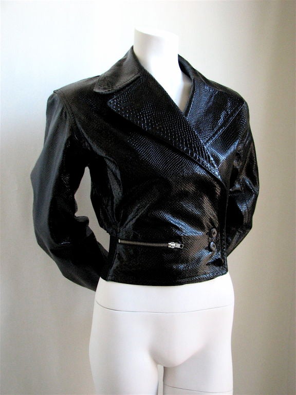 Black python embossed patent leather biker jacket with corset lace up detail at back. Silver zippered pocket at right hip. Asymmetrical triple button closure. Fully lined. FR 36. EXCELLENT CONDITION.