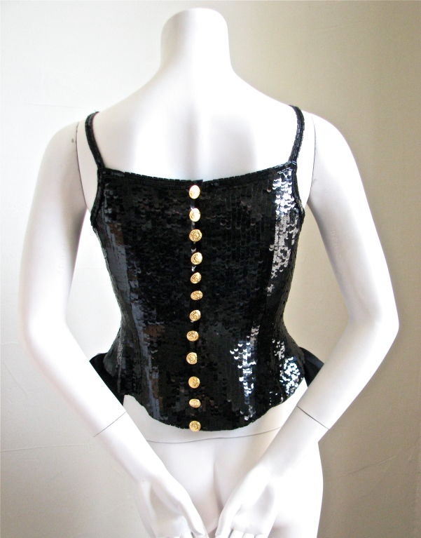 Very dramatic, jet black, sequined evening top trimmed with bugle beads and finished with large satin bows at hips. Secures at back with 12 shiny gilt metal buttons with interlocking 'CC' design. Fully lined in silk. Fits a US 2 or 4. Bust 33