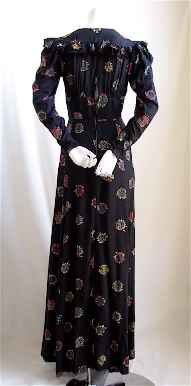 Ankle length dress with fitted bodice and empire waistline with print by Celia Birtwell made by Ossie Clark. Ca. 1970. Ruffles at shoulders and along top back. Princess sleeves with snaps at wrist. Deep V neckline. Peek-a-boo open back. Zips up