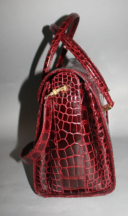 This gorgeous bag is constructed of firm burgundy alligator leather and features flat top handles and removable shoulder strap (replacement shoulder strap included). Flap top with turn key closure opens to burgundy leather lined main compartment